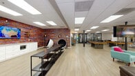 Located at 919 N Stone Ave in Tucson, Arizona, this single-floor community amenity space is designed to offer residents a dynamic and engaging environment for relaxation, recreation, and fitness. The interior is anchored by light wood-look flooring throughout, complemented by a drop ceiling with recessed panel lighting that keeps the atmosphere bright and welcoming.

The lounge area features large windows that invite natural light and offer views of the outdoor pool and surrounding greenery. Comfortable seating, including teal accent chairs, a large sectional sofa, and eclectic side tables, creates an inviting gathering space accented by vibrant Southwestern-themed artwork.

Adjacent to the lounge, the game room stands out with a bold, multicolored textured accent wall serving as a striking visual focal point. This area includes multiple pool tables, a wall-mounted television, a built-in kitchenette with white cabinetry and a beverage cooler, shelving units, and unique pod-style lounge chairs that add a playful, modern touch.

The fitness center is enclosed by sleek floor-to-ceiling glass walls and doors, providing full visibility into the well-equipped space featuring treadmills, cycling machines, and functional training equipment. Together, these amenities create a cohesive, energetic community hub suited for socializing and active living.