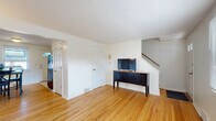 This two-story, 2-bedroom, 1-bathroom home at 6A Weis Rd in Albany, NY offers a practical and comfortable layout spread evenly across two floors. The main level features a bright living room with warm hardwood floors, a front entry door with sidelights, and a textured ceiling that adds character. Adjacent to the living area, the combined dining room and kitchen provides a functional flow. The kitchen is equipped with white cabinetry, black appliances including a gas range, over-the-range microwave, and a full-size refrigerator, alongside a stainless steel sink. The dining area accommodates a full table set and receives natural light from a window facing the entry door. Upstairs, both bedrooms continue the rich hardwood flooring theme. The spacious primary bedroom features two windows that invite ample natural light, while the second bedroom also includes a window with outdoor views and closet access. A hallway connects the upper-level rooms. The bathroom is a standout, showcasing retro-style mint green wall tiles with navy border accents, a mosaic tile floor, a tub-shower combo, wood vanity, and two windows for natural ventilation. Throughout the home, clean white walls and consistent hardwood floors create a cohesive, inviting atmosphere.
