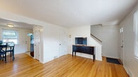 This two-story, 2-bedroom, 1-bathroom home at 6A Weis Rd in Albany, NY offers a practical and comfortable layout spread evenly across two floors. The main level features a bright living room with warm hardwood floors, a front entry door with sidelights, and a textured ceiling that adds character. Adjacent to the living area, the combined dining room and kitchen provides a functional flow. The kitchen is equipped with white cabinetry, black appliances including a gas range, over-the-range microwave, and a full-size refrigerator, alongside a stainless steel sink. The dining area accommodates a full table set and receives natural light from a window facing the entry door. Upstairs, both bedrooms continue the rich hardwood flooring theme. The spacious primary bedroom features two windows that invite ample natural light, while the second bedroom also includes a window with outdoor views and closet access. A hallway connects the upper-level rooms. The bathroom is a standout, showcasing retro-style mint green wall tiles with navy border accents, a mosaic tile floor, a tub-shower combo, wood vanity, and two windows for natural ventilation. Throughout the home, clean white walls and consistent hardwood floors create a cohesive, inviting atmosphere.