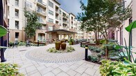 Located at 401 Oberlin Rd in Raleigh, NC, this meticulously designed outdoor amenity space serves as the centerpiece of a multi-story residential community. The courtyard is framed by an elegant multi-story building façade combining classic brick and neutral-toned siding, with private balconies overlooking the grounds on every level.

At the heart of the courtyard, a decorative circular paver plaza showcases a trio of large ceramic urn fountains nestled among river rock and lush landscaping, creating a tranquil focal point. The intricate cobblestone and tile paving patterns extend throughout the space, guiding visitors between distinct activity zones.

A covered pavilion with a pitched roof provides a shaded gathering area equipped with seating and outdoor grilling stations, ideal for communal use. Nearby, café-style tables and chairs offer additional seating options surrounded by manicured hedges and tropical plantings.

The resort-style swimming pool is a standout feature, with crystal-clear turquoise water and a generously sized pool deck lined with chaise lounges. Palm trees and well-maintained shrubs border the pool area, enhancing the resort ambiance. The building's grand entry features columned archways, potted tropical plants, and refined stonework, setting a polished tone throughout the entire outdoor space.