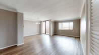 This single-floor residence offers a thoughtfully organized layout encompassing two bedrooms, two bathrooms, two living areas, a kitchen, a hallway, and two closets. The combined living and dining areas are generously proportioned, featuring rich hardwood-style flooring, neutral taupe walls, and crown molding that adds a refined architectural touch. An elegant chandelier anchors the dining area, while large windows and a sliding glass door flood the space with natural light and provide views of the surrounding outdoor scenery. The kitchen is efficiently designed with light wood cabinetry, white tile flooring, a tiled backsplash, and ample counter and storage space, accommodating all essential appliances. The primary bedroom is a spacious retreat finished with plush carpeting, while the second bedroom also features carpet and a wide window with outdoor views. Both closets offer practical storage, with one featuring classic louvered bi-fold doors. The two bathrooms are functionally appointed, each with a vanity, tub-shower combination, and tile flooring. A connecting hallway with recessed lighting links the rooms cohesively. Throughout, the space maintains a consistent, neutral color palette that creates a calm and welcoming ambiance.