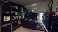 Located at 675 Evans St SW in Atlanta, GA, this single-floor home offers a distinctive and character-rich interior across several well-defined spaces. The living area serves as the centerpiece of the home, featuring dark-painted walls, vaulted ceilings, and recessed and track lighting that create a moody, dramatic atmosphere. Black leather sofas surround a glass-topped coffee table, while a large built-in entertainment and display unit lines one wall, showcasing decorative collectibles. A bold large-scale artwork adds visual depth to the space. Adjacent to the living area is a dining nook with warm wood tones, a classic china cabinet, and a chandelier overhead. The kitchen features dark wood cabinetry, dark countertops, a double-basin sink, and hardwood-style flooring, with a dedicated laundry area accessible through a connecting hallway. The bedroom is carpeted and comfortably sized, complete with a ceiling fan, closet with bifold doors, and rich wood furniture including a dresser and ornate bed frame. A full bathroom with hardwood-style flooring and a wood-toned vanity completes the layout. Throughout the home, personal artwork, textiles, and curated décor lend a lived-in warmth and individuality to every room.