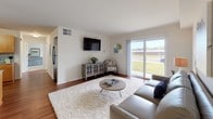 This single-floor, two-bedroom, one-bathroom residence offers a clean, modern design with a well-considered open layout. The living room serves as the heart of the home, featuring rich hardwood-style flooring, neutral white walls, and a sliding glass door that fills the space with natural light while providing views of the surrounding greenery outside.

The kitchen is thoughtfully appointed with warm honey-toned cabinetry, granite countertops, and a coordinating speckled tile backsplash. Black appliances, including a range, microwave, and dishwasher, complement the aesthetic, while a peninsula counter provides additional workspace and a natural division between the kitchen and living areas.

Both bedrooms are carpeted and offer a calm, neutral palette. The primary bedroom provides ample room for furnishings, while the second bedroom includes a built-in closet and a large window overlooking the outdoors. The shared bathroom features granite-topped cabinetry matching the kitchen's finishes, tile flooring, and a shower-tub combination. Throughout the unit, consistent finishes and a light color scheme create a cohesive and inviting atmosphere.