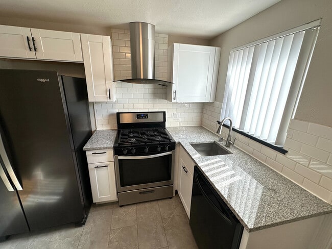 Modern kitchen with sleek granite countertops, stainless steel appliances, and elegant white cabinetry. - Flats at 16th