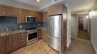 Located at 2000 E 9th St in the heart of Cleveland, Ohio, this thoughtfully designed single-floor residence combines modern finishes with functional living spaces. The kitchen serves as a standout feature, outfitted with rich warm-toned wood cabinetry, granite countertops, and a striking blue tile backsplash. Premium stainless steel appliances — including a French door refrigerator, electric range, built-in microwave, and dishwasher — complete the space, while large windows invite natural light and city views. Stone tile flooring runs throughout the kitchen, lending a clean, contemporary aesthetic. The bathroom continues the refined design language with a wide granite-topped vanity, warm wood cabinetry, an expansive mirror, and stone tile flooring. Chrome fixtures and dual towel rings add polished finishing touches, while a private water closet provides added convenience. The walk-in closet offers generous storage with multiple hanging rods and shelving, finished with soft carpeting underfoot. Neutral gray tones throughout the unit create a cohesive, modern atmosphere. The overall layout, as revealed in the floor plan view, is compact yet efficiently arranged, making excellent use of every square foot for comfortable urban living.