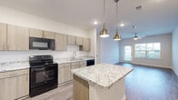 Located at 101 Pine Forest Rd in Augusta, Georgia, this single-story residence offers a thoughtfully designed layout with contemporary finishes throughout. The open-concept kitchen is a standout feature, equipped with light wood cabinetry, granite-patterned countertops, and a central island topped with striking veined granite. Black appliances — including a refrigerator, range, microwave, and dishwasher — complement the modern aesthetic, while pendant lighting with brass fixtures adds a warm, stylish touch. Wood-look flooring extends through the kitchen and living areas, creating a cohesive flow. The living space opens toward a private balcony, allowing natural light to filter through. The bedrooms are finished with plush carpeting and ceiling fans, and feature windows that provide pleasant outdoor views and ample natural light. Closet access is conveniently integrated into the bedroom layout. The bathrooms are clean and functional, featuring granite-topped vanities with light wood cabinetry, wood-look tile flooring, and tub-shower combinations with tiled surrounds. The overall design balances practicality with modern style, making this a well-appointed residence in the Augusta, GA area.