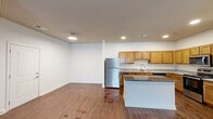 This single-floor residence is designed with a clean, modern aesthetic throughout. The open-concept kitchen and living area serves as the heart of the unit, featuring rich, dark hardwood-style flooring that extends seamlessly across the space. The kitchen is well-appointed with warm honey-toned cabinetry, granite countertops, and a full suite of stainless steel appliances, including a refrigerator and dishwasher. A central island with a dark granite surface provides additional prep space and visual contrast. Recessed lighting illuminates the kitchen and living areas, enhancing the bright, white walls that create a clean, airy atmosphere throughout.

The living area is generously sized, with a front entry door and a window that invites natural light into the space. The bedrooms are finished with plush neutral carpeting, white walls, and windows that overlook the outdoors, offering a calm and comfortable retreat. Raised panel doors add a subtle architectural detail to the interiors.

The bathroom is finished with the same consistent style, featuring a granite-topped vanity with warm wood cabinetry, a combined shower and tub with white tile surround, and hardwood-style flooring that ties the space together cohesively.