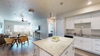 This thoughtfully designed 2-bedroom, 2-bathroom residence offers a practical and comfortable single-floor layout. The open-concept kitchen and living area serves as the heart of the home, anchored by a central granite-topped island with bar seating — ideal for casual dining or entertaining. White shaker cabinetry, stainless steel appliances, and pendant lighting give the kitchen a clean, modern aesthetic, while light wood-look flooring ties the space together seamlessly.

The living room is bright and welcoming, featuring large windows that invite generous natural light and a ceiling fan for year-round comfort. Neutral tones and a textured ceiling add warmth and depth to the space.

Both bedrooms are carpeted and well-sized, with ample natural light from windows dressed in blinds and drape panels. The primary bedroom connects to a private en-suite bathroom with a double-sink vanity, white cabinetry, and light quartz countertops. The second bathroom features a tub-shower combination with a single vanity, maintaining the same clean, contemporary style.

Two closets provide plentiful storage throughout the home. A dedicated in-unit laundry area houses a stacked washer and dryer, adding everyday convenience. The overall design palette — soft neutrals, crisp whites, and light wood tones — creates a cohesive and inviting atmosphere throughout.