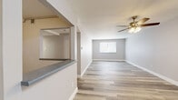 This 2-bedroom, 1-bathroom single-floor unit offers a clean, modern aesthetic with wood-look vinyl plank flooring that runs consistently throughout all rooms, complemented by neutral gray and beige wall tones and crisp white baseboards. The open layout connects two hallways that guide residents through the space efficiently.

The kitchen is well-appointed with white shaker-style cabinetry, granite-look countertops, a double stainless steel sink, and matching upper and lower cabinet storage — providing ample workspace and organization. A full-size refrigerator is included.

The living room is a generously sized open area that receives natural light through a window with outdoor views of surrounding greenery. Both bedrooms feature the same wood-look flooring and neutral tones, with windows that allow natural light to filter in. The primary bedroom offers a comfortable footprint, while the second bedroom includes closet access and additional window views.

The bathroom is neatly finished with a white shaker-style vanity, a framed mirror, a soaker tub-shower combination, and wood-look flooring that ties the space together. Throughout the unit, the consistent use of modern finishes and a neutral color palette creates a cohesive, move-in-ready living environment.