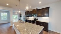 Located at 507 Merrion Park Ln in Morrisville, NC, this well-appointed three-story home offers a thoughtfully designed layout with modern finishes throughout. The heart of the home is an open-concept kitchen and living area, where rich dark-stained cabinetry with crown molding pairs beautifully with granite countertops and a classic white subway tile backsplash. A large center island with a double sink and decorative glass pendant lighting serves as both a functional workspace and a gathering point. Stainless steel appliances complete the kitchen's polished look. The adjoining living room features hardwood-style flooring, a fireplace with a white mantel, and abundant natural light from multiple windows. A set of French doors leads to an outdoor area, further enhancing the connection between indoor and outdoor living. The primary bathroom offers a spacious tiled walk-in shower with sliding glass doors and a vanity with ample storage. A secondary full bathroom includes a tub-shower combo and tile flooring. The carpeted bedroom features a tray ceiling with a ceiling fan and a large window with serene outdoor views. A dedicated laundry room with a full-size washer and dryer and built-in shelving adds everyday convenience to this move-in-ready home.