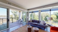 Located at 1700 Marinas Edge Way in Louisville, Kentucky, this single-floor residence offers a thoughtfully designed layout with contemporary finishes and abundant natural light. The open-concept living area is a standout, featuring expansive floor-to-ceiling windows and glass sliding doors that frame sweeping views of lush green treetops, creating a seamless indoor-outdoor connection. A private balcony accessible from the living room extends the living space outdoors. The living and dining areas flow together effortlessly, with a ceiling fan overhead and large windows that continue the light-filled atmosphere. The kitchen is a chef's highlight, boasting a substantial granite island with a built-in cooktop, stainless steel appliances, dark stone countertops, crisp white cabinetry, a tile backsplash, and overhead track lighting. The bedrooms are generously sized with plush carpeting and large windows overlooking the tree canopy, offering a tranquil retreat. A spacious walk-in closet provides ample built-in shelving and hanging storage. The bathrooms are well-appointed, featuring granite countertops, modern white cabinetry with tall storage towers, and a sleek glass-enclosed shower. Wood-look flooring runs throughout the main living areas, tying the modern aesthetic together cohesively.