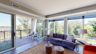 Located at 1700 Marinas Edge Way in Louisville, Kentucky, this single-floor residence offers a thoughtfully designed layout with contemporary finishes and abundant natural light. The open-concept living area is a standout, featuring expansive floor-to-ceiling windows and glass sliding doors that frame sweeping views of lush green treetops, creating a seamless indoor-outdoor connection. A private balcony accessible from the living room extends the living space outdoors. The living and dining areas flow together effortlessly, with a ceiling fan overhead and large windows that continue the light-filled atmosphere. The kitchen is a chef's highlight, boasting a substantial granite island with a built-in cooktop, stainless steel appliances, dark stone countertops, crisp white cabinetry, a tile backsplash, and overhead track lighting. The bedrooms are generously sized with plush carpeting and large windows overlooking the tree canopy, offering a tranquil retreat. A spacious walk-in closet provides ample built-in shelving and hanging storage. The bathrooms are well-appointed, featuring granite countertops, modern white cabinetry with tall storage towers, and a sleek glass-enclosed shower. Wood-look flooring runs throughout the main living areas, tying the modern aesthetic together cohesively.