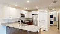This well-appointed single-floor unit offers a thoughtfully designed layout that balances functionality and modern aesthetics. The open-concept kitchen serves as the centerpiece, showcasing crisp white upper cabinetry paired with rich dark wood lower cabinets and a light quartz countertop. A large kitchen island with an undermount sink and seating overhang provides additional workspace and casual dining. Stainless steel appliances, including a refrigerator, electric range, and built-in microwave, complete the contemporary look, while recessed lighting illuminates the space throughout.

The living area features light wood-look flooring and benefits from natural light entering through a door with an adjacent sidelight window, creating a bright and welcoming atmosphere. A connecting hallway with the same wood-look flooring leads to the private areas of the unit.

The bedrooms are finished with plush neutral carpet, offering a comfortable and quiet retreat. One bedroom includes a window that brings in natural light. The bathroom is clean and functional, featuring a full tub-and-shower combination with built-in shelving and chrome fixtures set against bright white surroundings. Throughout the unit, neutral tones, white panel doors, and consistent finishes create a cohesive and modern living environment.