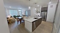 This 890-square-foot, single-floor apartment at 13959 Hillcroft, Unit 1103, features 2 bedrooms, 2 bathrooms, and a well-planned open layout. The living room is bright and inviting, filled with natural light from large windows with horizontal blinds, and features light wood-style flooring and recessed lighting. The kitchen is outfitted with dark wood-grain cabinetry extending to the ceiling, white quartz countertops, stainless steel appliances including a range, built-in microwave, and refrigerator, plus a textured tile backsplash and a built-in desk nook. The primary bedroom measures 150 square feet and includes a ceiling fan, expansive windows, and a dedicated walk-in closet with wire shelving and hanging rods. The second bedroom also benefits from natural light via a large window. Both bathrooms feature dark wood-grain vanity cabinetry, white quartz countertops, and tile work. The primary bath includes a glass-enclosed shower, while the second bath offers a soaking tub with tiled surround and shower curtain. Light wood-style flooring flows throughout the unit, complementing the clean, neutral color palette and creating a cohesive, modern aesthetic across all rooms.