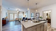 Located at 171 Town Park Drive in Conroe, Texas, this single-floor residence offers a thoughtfully designed open-concept layout that seamlessly connects the kitchen, dining, and living areas. The kitchen is a standout feature, showcasing granite countertops, taupe cabinetry with gold hardware, stainless steel appliances including a range, microwave, and dishwasher, and a central island with a stainless steel sink and elegant pendant lighting overhead. Light wood-style flooring flows throughout the main living areas, enhancing the bright, airy ambiance. The living room is a comfortable and inviting space, highlighted by a ceiling fan, large windows, and French doors that open to a private balcony, allowing abundant natural light to fill the room. The bedroom features plush carpeting, multiple windows with exterior views, a ceiling fan, and direct access to a spacious walk-in closet with built-in shelving and hanging rods. Additional closet storage is also available. The bathroom is well-equipped with granite countertops, a single undermount sink, taupe cabinetry, a large mirror, and a glass-enclosed shower, all finished with the same wood-style flooring found throughout. This residence combines functional design with refined finishes throughout.