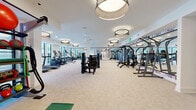 Located at 3712 Stewart Rd in Doraville, GA, this modern fitness center offers a generously sized, single-floor exercise space designed to support a full range of workout routines. The open floor plan is finished with neutral carpeting throughout and bright white walls, creating a clean, inviting atmosphere. Stylish drum pendant light fixtures and ceiling fans are distributed evenly across the space, ensuring comfortable airflow and consistent illumination.

The main area houses a comprehensive selection of strength training machines, including cable systems, plate-loaded equipment, and selectorized machines, alongside a dedicated free weights section featuring a full dumbbell rack with benches and floor-to-ceiling mirrors. A row of cardio machines, including treadmills and ellipticals, lines one wall, benefiting from natural light provided by large windows with views of the outdoors.

A distinct functional training zone features eye-catching, artistically patterned accent wallpaper and is stocked with a well-organized equipment rack holding kettlebells, medicine balls, resistance bands, foam rollers, and stability balls. This area also includes open floor space with a yoga mat, ideal for stretching and bodyweight exercises. The thoughtful layout and diverse equipment selection make this fitness center a comprehensive resource for users of all fitness levels.
