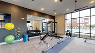 Located in Westerville, Ohio, this modern fitness center is designed to support a comprehensive workout experience across a single, open-plan floor. The space is divided into distinct functional zones, each thoughtfully arranged to maximize usability and flow.

The cardio area lines the windowed perimeter wall, where multiple treadmills, elliptical machines, and a rowing machine are positioned to take advantage of generous natural light and outdoor views. Ceiling fans overhead and wall-mounted televisions provide comfort and entertainment during cardio sessions.

The strength training zone features a full rack of dumbbells displayed on tiered stands, a power rack, adjustable benches, and a Bodycraft cable machine offering a variety of resistance exercises. A large wall-to-wall mirror spans this area, enhancing the sense of space and allowing users to monitor their form.

A functional training section rounds out the facility, equipped with medicine balls, stability balls, and open floor space for stretching or bodyweight exercises. The flooring throughout combines durable carpet tile with rubberized mat sections suited for lifting and dynamic movement.

The design aesthetic is clean and contemporary, with dark accent walls contrasting against light-toned surfaces and recessed lighting. Large steel-framed windows and glass panels invite natural light throughout the space, creating an energizing and motivating environment for all fitness levels.