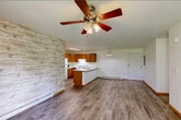 Located at 830 Union Street in Platteville, WI, this single-floor, 4-bedroom, 2-bathroom home offers a practical and comfortable layout. The combined kitchen and living room serves as the heart of the home, featuring durable hardwood-style flooring, a striking whitewashed stone accent wall, and a ceiling fan overhead. The kitchen is equipped with warm wood cabinetry, white appliances including a refrigerator and range, and a peninsula with a built-in sink and pendant lighting — ideal for both cooking and casual dining. Sliding glass doors in the living area open to a private patio, filling the space with natural light and providing views of the lush, tree-lined yard beyond a white fence. Each of the four bedrooms is carpeted for comfort, fitted with a ceiling fan, and includes a window that brings in natural light. Five closets throughout the home offer generous storage. The two bathrooms are clean and functional, featuring tiled tub surrounds and hardwood-style flooring. Baseboard heating is present throughout. The exterior grounds are well-maintained, with mature trees providing shade and a peaceful residential setting in Platteville.