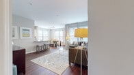 This thoughtfully designed single-floor residence offers a seamless blend of comfort and modern style. The open-concept layout connects the living and dining areas, creating a bright, airy atmosphere enhanced by abundant natural light streaming through multiple large windows dressed with elegant drapes and blinds. Rich hardwood-style flooring flows throughout the main living spaces, adding warmth and cohesion to the design.

The living room is a welcoming retreat, featuring a generously sized sectional sofa, glass-top coffee tables, and a classic area rug that anchors the space. The adjoining dining area is bathed in natural light from a bank of windows and is illuminated by stylish track lighting overhead, making it ideal for both everyday meals and entertaining.

The galley kitchen is efficiently laid out with crisp white cabinetry, gray countertops, stainless steel appliances — including a gas range, microwave, refrigerator, and dishwasher — and a decorative arabesque tile backsplash that adds a refined touch.

The primary bedroom offers a serene escape with plush carpeting, large windows, and ample space, complemented by an en-suite bathroom featuring a long vanity with warm wood cabinetry. A second well-proportioned bedroom also features soft carpeting and generous natural light. A secondary bathroom includes a full soaking tub with tiled surround, completing this comfortable and functional residence.