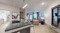 This well-appointed single-floor residence at 13645 E Colonial Dr in Orlando, Florida offers a cohesive blend of modern design and functional living. The open-concept layout seamlessly connects the kitchen, dining, and living areas, creating a bright and welcoming atmosphere enhanced by light wood-style flooring throughout.

The contemporary kitchen is a standout feature, showcasing dark granite countertops, a large center island with bar seating, light wood cabinetry, a classic subway tile backsplash, and a full suite of stainless steel appliances including a refrigerator, electric range, microwave, and dishwasher. Pendant and track lighting add a polished finishing touch.

The living area is generously proportioned, featuring a ceiling fan, large windows with teal drape accents that invite natural light, and a wall-mounted flat-screen TV. The space comfortably accommodates multiple seating arrangements and exudes a relaxed, contemporary ambiance.

The bedroom offers a tranquil retreat with plush carpeting, natural light from blinds-fitted windows, and a spacious walk-in closet outfitted with wire shelving and hanging rods for ample storage.

The bathroom is finished with the same light wood-style flooring, a dark granite vanity countertop, wood-toned cabinetry, a large mirror, and a separate shower, providing a clean and modern feel throughout.