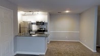 Located at 997 Johnnie Dodds Boulevard in Mount Pleasant, South Carolina, this single-floor residence offers a thoughtfully designed open-concept layout that seamlessly connects the kitchen and living areas. The kitchen is outfitted with a full suite of stainless steel appliances, including a refrigerator, range, and built-in microwave, complemented by sleek granite countertops and crisp white cabinetry. A peninsula-style counter provides additional workspace and serves as a natural divider between the kitchen and the adjoining living space. Track lighting overhead ensures the kitchen is well-lit and functional. The living area features neutral-toned carpeting that adds warmth underfoot, while the light gray walls and white chair rail molding contribute a clean, classic aesthetic. Recessed lighting further brightens the space. The open flow between rooms creates a welcoming and versatile environment, well-suited for both everyday living and entertaining. The overall design balances practicality with modern style, making efficient use of the single-floor footprint in this conveniently located Mount Pleasant property.