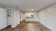 This single-story, 1-bedroom, 1-bathroom unit offers a thoughtfully designed open-concept layout with a neutral color palette and clean finishes throughout. The living room is a standout space, featuring wood-look luxury vinyl flooring, a classic fireplace, and a large sliding glass door with vertical blinds that floods the room with natural light and provides access to an outdoor area. A textured ceiling adds character to the living space.

The kitchen is accessed via a pass-through counter that also serves as a breakfast bar, making it an ideal feature for casual dining or entertaining. Inside the kitchen, white cabinetry pairs with granite-look countertops, a stainless steel sink, and black appliances including a range, microwave, dishwasher, and full-size refrigerator. Wood-look flooring continues throughout the kitchen, maintaining a cohesive design.

The bedroom is carpeted for comfort and includes a ceiling fan, a window with an outdoor view, and a dedicated closet. The bathroom features a full tub-shower combo with tiled surround, wood-look flooring, and a vanity with granite-look countertops. Additional storage is provided by a separate closet accessible from the main living area, completing this functional and well-finished single-floor residence.