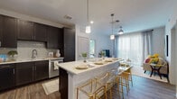 This single-story residence showcases a thoughtfully designed open-concept layout that seamlessly connects the kitchen and living areas. The kitchen is a standout feature, equipped with dark espresso cabinetry, a subway tile backsplash, stainless steel appliances, and a generously sized white quartz island with bar seating. Pendant lighting above the island adds a modern touch, while wood-look flooring extends throughout the main living area. Built-in shelving near the kitchen provides additional display and storage space. A sliding glass door leads to an outdoor balcony, filling the living area with natural light.

The multiple bedrooms are carpeted for comfort and each include ceiling fans, large windows with sheer curtains, and ample natural light. Each room offers a calm, well-lit retreat with neutral and accent wall tones.

The bathrooms maintain the design continuity with large-format light tile flooring, dark cabinetry with white countertops, and clean white walls. The primary bathroom features a dual-sink vanity with an elongated layout, providing generous counter and storage space. The secondary bathroom includes a single vanity with a tub-shower combination, finished with white subway tile.