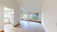 Located at 515 S 152nd St in Burien, Washington, this 2-bedroom, 1-bathroom unit offers a well-designed single-floor layout with a bright, open feel. The living room is a standout space, featuring soaring vaulted ceilings, a ceiling fan, and a wide bank of large windows that frame lush views of Pacific Northwest evergreen trees, filling the room with natural light. Light-toned laminate wood flooring runs throughout the entire unit, lending a clean and cohesive aesthetic.

The kitchen is efficiently arranged in a galley style, outfitted with crisp white shaker cabinetry, quartz countertops, a stainless steel sink, and stainless steel appliances including a refrigerator and range. A window above the sink adds additional natural light to the workspace.

The primary bedroom is generously proportioned and features a large picture window overlooking the surrounding greenery, along with vaulted ceilings that enhance the sense of space. The second bedroom includes two windows with blinds and the same warm laminate flooring. The full bathroom is clean and functional, featuring a quartz-topped vanity with white cabinetry, a full soaking tub with shower, and consistent laminate flooring. A hallway connects the rooms, completing this efficient and comfortable layout.