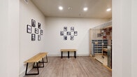 Located at Heritage Towne Blvd in Midlothian, TX, this single-floor wellness suite is thoughtfully designed to deliver a focused sauna and relaxation experience. The space is organized around two key areas: a hallway lounge and a bathroom, complemented by a centerpiece Clearlight infrared sauna enclosure.

The hallway lounge sets a calm, welcoming tone with crisp white walls, light wood-look luxury vinyl plank flooring, and recessed ceiling lighting. Two natural wood benches with black metal legs provide comfortable seating, while a curated gallery of black-and-white dog portrait photographs adds a warm, personable character to the walls. A storage organizer, yoga mat, and potted greenery are also present, reinforcing the wellness-oriented atmosphere.

The Clearlight infrared sauna dominates the space with its light-toned wood paneling, integrated infrared heating panels, and glass door entry. A digital control panel allows users to customize their session settings with ease. The sauna's clean, modern construction reflects a high-quality, purpose-built wellness installation.

The bathroom provides essential amenities to support the overall wellness experience. Together, the elements of this suite create an intimate, professionally appointed environment ideal for infrared sauna therapy and personal recovery sessions.