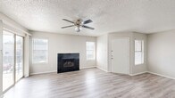 Located at 1595 S Old Orchard Ln in Lewisville, TX, this single-floor, one-bedroom residence offers a well-organized layout designed for comfortable everyday living. The open living room serves as the heart of the home, featuring light wood-style flooring, a textured ceiling, a ceiling fan with light fixture, and a striking black-tiled fireplace as a focal point. Multiple windows allow natural light to fill the space, and a sliding glass door provides direct access to an outdoor patio area. The kitchen is positioned adjacent to the living area and is accessible via a pass-through opening framed by a granite-topped breakfast bar. Dark wood cabinetry, a white refrigerator, and a range with overhead ventilation complete the kitchen. The bedroom is a well-proportioned private retreat with its own ceiling fan, a window for natural light, and direct access to a bathroom visible through a connecting doorway. A dedicated laundry area includes wire shelving and a water heater, keeping utility functions neatly contained. A hallway and closet complete the layout, offering practical storage solutions. Consistent light-toned wood-style flooring and a neutral color palette throughout create a cohesive, clean aesthetic.