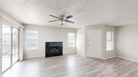 Located at 1595 S Old Orchard Ln in Lewisville, TX, this single-floor, one-bedroom residence offers a well-organized layout designed for comfortable everyday living. The open living room serves as the heart of the home, featuring light wood-style flooring, a textured ceiling, a ceiling fan with light fixture, and a striking black-tiled fireplace as a focal point. Multiple windows allow natural light to fill the space, and a sliding glass door provides direct access to an outdoor patio area. The kitchen is positioned adjacent to the living area and is accessible via a pass-through opening framed by a granite-topped breakfast bar. Dark wood cabinetry, a white refrigerator, and a range with overhead ventilation complete the kitchen. The bedroom is a well-proportioned private retreat with its own ceiling fan, a window for natural light, and direct access to a bathroom visible through a connecting doorway. A dedicated laundry area includes wire shelving and a water heater, keeping utility functions neatly contained. A hallway and closet complete the layout, offering practical storage solutions. Consistent light-toned wood-style flooring and a neutral color palette throughout create a cohesive, clean aesthetic.