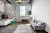 Unit 2081 at 11900 Main St in Fredericksburg, Virginia, is a single-floor loft that masterfully blends industrial character with contemporary finishes. The open living area makes a striking first impression with its soaring ceilings, large factory-style multi-pane windows that flood the space with natural light, and polished concrete floors that carry throughout the unit. Exposed white-painted brick walls add texture and a nod to the building's industrial heritage.

The kitchen is both functional and stylish, featuring gray shaker cabinetry, granite countertops, a full suite of stainless steel appliances including a range, microwave, dishwasher, and refrigerator, and a peninsula with bar seating beneath pendant lighting — ideal for casual dining or entertaining.

The bedroom is generously proportioned with the same dramatic ceiling height, abundant natural light from industrial-style windows, and dual sliding-door closets providing ample storage. The bathroom offers a clean, modern aesthetic with large-format tile surrounding the tub and shower, a granite-topped vanity, and gray cabinetry consistent with the kitchen's design language.

Throughout the unit, bold navy-painted doors and trim provide a cohesive design accent against the crisp white walls and raw concrete, creating a space that is both refined and distinctly urban in character.