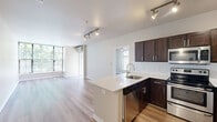 This thoughtfully designed 2-bedroom, 2-bathroom residence offers a functional and modern living experience across a single floor. The open-concept layout seamlessly connects the kitchen and living room, creating a bright and cohesive common area anchored by light wood-tone flooring that runs throughout the space.

The kitchen is a standout feature, equipped with dark espresso cabinetry, a classic white subway tile backsplash, stainless steel appliances including a refrigerator, range, and microwave, and a generous island with a marble-style quartz countertop and undermount sink. Track lighting overhead adds both task illumination and a contemporary touch.

The living area benefits from expansive floor-to-ceiling windows that invite generous natural light and offer views of surrounding greenery. A glass exterior door provides additional brightness and outdoor access. A wall-mounted HVAC unit ensures year-round climate comfort.

The primary bedroom is a well-proportioned retreat with large windows framing leafy outdoor views. Both bedrooms feature the same consistent wood-tone flooring and neutral wall tones, complemented by dedicated closets with wire shelving systems for organized storage.

The bathrooms are clean and functional, featuring light wood-tone flooring, a shower/tub combination, and straightforward, understated fixtures. The overall design palette throughout the residence is neutral and modern, offering a versatile canvas for personalization.