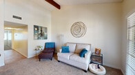 Located at 5666 E Hampton St in Tucson, Arizona, this single-story residence offers a thoughtfully arranged layout with a warm, inviting ambiance throughout. The living room is a standout space, featuring soaring vaulted ceilings accented by a prominent exposed wood beam, creating a sense of openness and architectural character. Neutral-toned carpet flows underfoot, while bright white walls provide a clean backdrop. French doors flood the area with natural light and provide direct access to an outdoor balcony area, offering a seamless indoor-outdoor connection. A wall-mounted television and hardwood flooring near the entry add both function and style to this gathering space. The dining area accommodates a round wooden table with seating for four, complemented by a ledge and adjacent storage. The bedroom is carpeted and comfortably scaled, featuring a large window with blinds that allow for ample natural light, along with a closet for storage. A second bedroom mirrors this comfort with its own closet and soft lighting. Throughout the home, a consistent neutral color palette and textured ceilings contribute to a cohesive, livable atmosphere well-suited to the sunny Tucson climate.