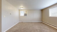 Located at 1037 Mary St in Emporia, Kansas, this compact single-floor unit offers two bedrooms, one bathroom, a kitchen, and a closet within an efficiently organized layout. The spacious primary bedroom occupies a substantial portion of the total floor area, featuring neutral-toned carpeting, beige walls, and multiple windows fitted with blinds that allow natural light to filter in. A window-mounted air conditioning unit provides cooling, while baseboard heating runs along the perimeter walls for warmth. The second bedroom mirrors this functional design with carpeted flooring, a baseboard heater, and a window for natural light.

The living area is carpeted and opens toward a compact kitchen equipped with white cabinetry, light countertops, a coil-burner electric range, and a refrigerator. Tile flooring in the kitchen adds a practical contrast to the carpeted living spaces. The bathroom features a wood-toned vanity with a single sink, a tub-shower combination with a molded surround unit offering built-in shelving, and tile flooring. Throughout the unit, the palette remains consistently light and neutral, contributing to a simple, utilitarian ambiance suited for straightforward, comfortable living.
