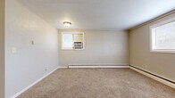 Located at 1037 Mary St in Emporia, Kansas, this compact single-floor unit offers two bedrooms, one bathroom, a kitchen, and a closet within an efficiently organized layout. The spacious primary bedroom occupies a substantial portion of the total floor area, featuring neutral-toned carpeting, beige walls, and multiple windows fitted with blinds that allow natural light to filter in. A window-mounted air conditioning unit provides cooling, while baseboard heating runs along the perimeter walls for warmth. The second bedroom mirrors this functional design with carpeted flooring, a baseboard heater, and a window for natural light.

The living area is carpeted and opens toward a compact kitchen equipped with white cabinetry, light countertops, a coil-burner electric range, and a refrigerator. Tile flooring in the kitchen adds a practical contrast to the carpeted living spaces. The bathroom features a wood-toned vanity with a single sink, a tub-shower combination with a molded surround unit offering built-in shelving, and tile flooring. Throughout the unit, the palette remains consistently light and neutral, contributing to a simple, utilitarian ambiance suited for straightforward, comfortable living.