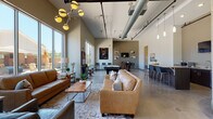 Located at 5437 Bowman Rd in Macon, Georgia, this single-floor community clubhouse showcases a contemporary industrial-modern design characterized by soaring vaulted ceilings, exposed ductwork, and polished concrete floors throughout. The open-concept layout is flooded with natural light courtesy of expansive floor-to-ceiling windows that frame views of the surrounding outdoor grounds and pool area.

The main lounge is a generously proportioned gathering space anchored by plush leather sofas, layered area rugs, and a striking sputnik chandelier alongside track lighting. The area flows seamlessly into a dedicated billiards zone, where a full-size pool table sits beneath tall windows overlooking a landscaped patio, with curated artwork adorning the walls.

A well-appointed kitchenette bar provides a central gathering point, featuring a granite-topped island with seating for several, dark wood cabinetry, a wall-mounted television, and countertop appliances — ideal for casual entertaining or refreshment breaks.

A designated office or leasing area near the entrance offers workstation seating, wall-mounted displays, and decorative accents, providing a functional yet stylish space for administrative purposes. The reception area greets visitors with an open, airy feel, complemented by additional seating clusters and direct access to the outdoors. The overall ambiance is welcoming, modern, and well-suited for community gatherings and daily use.