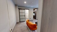 Located at 523 Main St in downtown Hartford, CT, this thoughtfully designed one-bedroom, one-bathroom residence offers a efficient yet comfortable single-floor layout. The living room is a welcoming focal point, featuring large windows that invite natural light and offer views of the surrounding neighborhood. The space is finished with neutral tones, recessed lighting, and polished tile flooring that flows throughout, lending a clean and cohesive aesthetic. A contemporary kitchen is equipped with dark cabinetry, a built-in cooktop, and a compact footprint that maximizes functionality. The bedroom provides a comfortable retreat, featuring built-in wardrobe storage with modern wood-paneled doors, wall-mounted artwork, and ample room for furnishings. The bathroom is a standout feature, appointed with stone-tiled walls surrounding a soaking tub and a striking multi-function tower shower panel, complemented by matte black hardware and stone-look flooring. A sleek frosted-glass sliding barn door connects the living area to the bathroom, adding a modern industrial touch. The unit also includes a dedicated closet for additional storage. Overall, the space blends urban sophistication with practical design throughout.