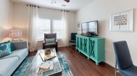 This single-floor residence offers a thoughtfully designed layout that balances comfort and functionality across its key living spaces. The kitchen is a standout, featuring warm-toned wood cabinetry, granite countertops, stainless steel appliances including a range and over-the-range microwave, and rich hardwood flooring. A breakfast bar with pendant lighting overhead provides a casual dining option, seamlessly connecting the kitchen to the rest of the living area. The living room is bright and welcoming, with wide windows dressed in layered curtains and blinds that allow ample natural light to filter in. Hardwood floors extend throughout the main living space, adding warmth and visual continuity. The bedrooms are carpeted for comfort and feature windows that bring in natural light. Each bedroom is well-sized, with one including a ceiling fan. An adjacent hallway connects the bedrooms to the shared bathroom, which includes a full soaking tub with shower, a single vanity with warm wood cabinetry and granite countertop, tile flooring, and a large framed mirror with overhead lighting. Throughout the space, neutral wall tones and clean finishes create a cohesive, modern ambiance suited for everyday living.