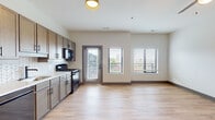 The Topaz unit in Louisville, KY offers a thoughtfully designed single-floor layout that combines modern aesthetics with functional living. Light wood-style flooring flows consistently throughout, creating a cohesive and clean visual identity across every room.

The open-concept kitchen and living area serves as the heart of the unit. The kitchen features warm-toned cabinetry with matte black hardware, a herringbone-patterned tile backsplash, light countertops, and black stainless appliances including a gas range, dishwasher, microwave, and refrigerator. A door from the kitchen opens directly to an outdoor space, and large windows frame views of the surrounding cityscape, filling the area with natural light.

A well-proportioned hallway connects the main living area to the private spaces, lined with dark-framed doors that add contemporary contrast to the neutral walls. The bedroom is generously sized, featuring a ceiling fan, vaulted ceiling detail, and a sliding-door closet with built-in shelving for ample storage.

The bathroom is finished with large-format marble-look tile flooring, a full soaking tub with subway tile surround, matte black fixtures, and a vanity with matching cabinetry, delivering a polished and cohesive design.