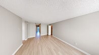 Located at 5810 Amaya Dr, Unit 16A in La Mesa, California, this single-floor residence offers a well-organized layout with a cohesive, neutral design palette throughout. Light wood-style flooring flows consistently across the main living areas and bedrooms, complemented by crisp white baseboards and soft gray walls that lend the space a clean, contemporary feel.

The open living area is generously proportioned, featuring a textured popcorn ceiling and a long hallway that connects the various rooms, drawing natural light from a glazed entryway door at the far end. A dedicated bedroom features mirrored sliding closet doors that maximize the sense of space, along with a wide window that frames views of the surrounding greenery. Additional rooms provide window-lit spaces well-suited for sleeping or home office use.

The kitchen is a functional highlight, equipped with white shaker-style cabinetry, dark granite countertops, and a full suite of stainless steel appliances including a refrigerator, range with electric cooktop, microwave, and dishwasher. Light wood flooring and recessed lighting complete the polished look.

The bathroom includes a granite-topped vanity with white cabinetry, a large mirror with overhead lighting, a walk-in shower with glass doors, and a toilet, all finished in a consistent neutral tone. Built-in storage cabinetry is also visible in the hallway area, adding practical utility to the overall layout.