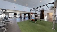 Located at 1763 S Kipling Pkwy in Lakewood, Colorado, this single-story fitness center is a comprehensively outfitted facility designed to support a wide range of workout styles and fitness goals. The space is organized into several distinct functional zones, each tailored to a specific type of training.

The strength training area is expansive, featuring rubber flooring, a power rack with a suspended heavy bag, barbells, weight plates, medicine balls, and a turf section ideal for functional training drills. Dumbbell racks and multiple selectorized cable and resistance machines line the mirrored walls, which are accented by bold yellow panels that add visual energy to the space. Large windows provide natural light and views of the surrounding outdoor areas, including a tennis court visible from one vantage point.

The cardio section houses a row of treadmills and elliptical trainers positioned near windows, with wall-mounted televisions for entertainment. Dark accent walls and recessed lighting create a focused atmosphere, while exposed ductwork adds an industrial touch to the vaulted ceiling areas.

A separate spin studio features light wood flooring, cycling bikes, built-in cabinetry, and a mounted television, offering a bright and clean environment for group or solo cycling sessions. Throughout the facility, the design balances functionality with a modern aesthetic, making it a well-rounded fitness destination.