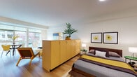 This thoughtfully designed single-floor unit offers a cohesive, modern aesthetic defined by warm light wood flooring, clean white walls, and an abundance of natural light throughout. The open-concept living and dining area is anchored by large floor-to-ceiling windows that frame street-level views and bathe the space in daylight. The living area provides generous room for both lounging and dining, with a seamless flow that makes the layout feel airy and expansive. Adjacent to the living space, the kitchen is efficiently designed with light maple cabinetry, stainless steel appliances including a refrigerator, gas range, microwave, and dishwasher, plus light-toned countertops that complement the overall warm palette. A peninsula-style storage cabinet with matching maple finishes serves as a stylish room divider, elegantly separating the living area from the bedroom. The bedroom is a calm, well-proportioned retreat that benefits from natural light and features the same warm hardwood flooring. The bathroom is finished with a wide vanity, maple cabinetry, stone-toned countertops, and a full mirror, maintaining the clean and consistent design language found throughout the unit. Overall, the space exudes a mid-century modern sensibility with a warm, inviting ambiance.