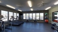 This fitness center offers a dedicated space for exercise and wellness, thoughtfully designed to support a variety of workout routines. The room features dark, durable flooring that provides both stability and easy maintenance, ideal for high-traffic use. Multiple large windows line the walls, allowing ample natural light to fill the space and offering views of the surrounding outdoors, creating an open and energizing atmosphere. Ceiling fans help maintain comfortable airflow throughout the room.

The cardio section is well-appointed, featuring a row of treadmills along one wall, complemented by upright stationary bikes positioned toward the center of the room. Exercise balls are available for stretching and core workouts, adding versatility to the space. A wall-mounted flat-screen television provides entertainment during workouts.

Overhead fluorescent lighting ensures the space remains bright even in low-light conditions. The neutral, dark-toned walls contribute to a focused and functional environment. Overall, this fitness center is a practical and well-organized facility that caters to residents looking to maintain an active lifestyle without leaving the property.