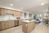 This thoughtfully designed single-floor residence showcases a clean, contemporary aesthetic throughout, with light wood-tone finishes, white walls, and light hardwood-style flooring that create a bright and cohesive atmosphere. The open-concept layout seamlessly connects the kitchen, dining, and living areas, making the space feel expansive and welcoming. The kitchen is well-equipped with warm wood-grain cabinetry extending to the ceiling, white quartz countertops, stainless steel appliances including a range, microwave, dishwasher, and refrigerator, and a central island that provides additional prep space and storage. The living area is generously proportioned, bathed in natural light through large windows that frame outdoor views, and offers ample room for comfortable seating and a dedicated workspace. The bedroom is a serene retreat, featuring a large window that continues the theme of natural light, direct sightlines to the kitchen, and built-in closet space. A spacious walk-in closet with built-in shelving and hanging rods provides excellent storage. The bathroom completes the unit with a wood-vanity, white quartz countertop, undermount sink, and a full soaking tub with subway-tiled surround. The overall ambiance is modern, airy, and well-balanced.