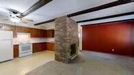 Located at 417 Seventh St N in Sartell, Minnesota, this two-bedroom, one-bathroom single-floor home offers a thoughtfully laid-out interior with several distinctive architectural details. The combined kitchen and living area serves as the heart of the home, anchored by a striking full-height brick fireplace that divides the space and adds rustic character. Exposed dark wood ceiling beams run throughout, complementing the textured ceiling and adding warmth to the open layout. A ceiling fan and wall-mounted AC unit provide comfort year-round. The kitchen features ample warm-toned wood cabinetry wrapping the perimeter, white appliances including a range and full-size refrigerator, a double sink, and light vinyl flooring. The living area is carpeted and benefits from a sliding glass door that brings in natural light and provides exterior access. Both bedrooms are carpeted and finished with neutral tones, offering a calm and functional retreat. The primary bedroom includes a large double-door closet with warm wood trim. Baseboard heating is present throughout the home. The bathroom features a full tub and shower enclosure with clean white tile surround. A connecting hallway ties the rooms together efficiently, completing this well-organized single-floor layout.