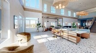 Located at 18750 Delaware St in Huntington Beach, California, this expansive two-floor amenity space blends coastal modern design with carefully curated interiors across a generous footprint. The main level commands attention with soaring double-height ceilings lined by clerestory windows that flood the space with abundant natural light and offer open views of the surrounding Huntington Beach skyline. Polished terrazzo flooring anchors the central gathering areas, transitioning to light wood floors throughout, while warm natural wood beams and trim add architectural warmth throughout.

The main level is organized into distinct yet open zones, including lounge seating with plush, sculptural furniture, intimate booth-style nooks framed by lush greenery, a large communal bar with pendant lighting and high seating, and a kitchenette with light wood cabinetry, stone counters, and a tile backsplash. Oversized sliding glass doors open directly to an outdoor pool area, seamlessly connecting interior and exterior living.

The upper level offers a more intimate retreat, featuring a built-in media wall with a bold botanical wallcovering, a wet bar, a dedicated lounge area, and a decorative pendant divider that frames sweeping outdoor views. A dramatic staircase with a living plant installation beneath it connects both floors, completing the space's resort-inspired, coastal aesthetic.