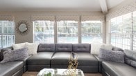 This well-appointed single-floor space showcases a cohesive contemporary design throughout, highlighted by warm wood-look flooring, neutral toned walls, and vaulted ceilings that lend an airy, open feel to the layout.

The kitchen is a standout feature, offering dark espresso cabinetry paired with granite countertops, stainless steel appliances, and a spacious island with seating for multiple bar-height chairs. Pendant lighting hangs above the island, and track lighting accents the soaring ceiling, creating a bright and functional workspace that flows seamlessly into the surrounding living areas.

The main living area is generously sized, anchored by a large sectional sofa and framed by a bank of windows that invite natural light and outdoor views, including a glimpse of a pool area beyond. A second, more intimate sitting room provides additional lounge space, featuring a wall-mounted television, a sleek media console, and a mix of modern seating.

The dining area benefits from its own vaulted ceiling and an interior glass door that connects to an adjacent room, enhancing the sense of depth and flow. A round glass dining table with upholstered chairs occupies the center of the space.

Overall, the layout is thoughtfully arranged, with distinct yet interconnected zones that balance openness with purposeful design.