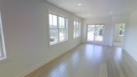 This single-floor space showcases a clean, modern design characterized by an open layout and a bright, airy atmosphere. The main living area is finished with light-toned hardwood flooring that runs throughout, reflecting natural light and contributing to the overall sense of spaciousness. Crisp white walls provide a neutral backdrop that enhances the room's luminosity.

A prominent feature of the space is the generous fenestration along one wall, where two large double-hung windows allow abundant daylight to stream in, offering views of the surrounding greenery and neighborhood streetscape. Adjacent to the windows, a full-lite glass door opens to an outdoor area, further connecting the interior to the exterior environment and adding an additional source of natural light.

Recessed ceiling lighting complements the natural light, ensuring the space remains well-illuminated at all times. White baseboards and window trim add a polished, cohesive finish to the interior. The overall ambiance is fresh and contemporary, making the space feel welcoming and versatile, well-suited for a variety of uses and furnishing arrangements.