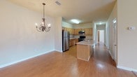 This single-floor home offers a thoughtfully designed open-concept layout that connects the kitchen and dining area seamlessly. The kitchen is equipped with warm oak cabinetry, generous counter space with light countertops, stainless steel appliances including a refrigerator and range, and a central island with a sink — ideal for both cooking and casual dining. An elegant chandelier anchors the adjacent dining area, which flows over durable hardwood-style flooring.

The spacious living room is a standout feature, boasting vaulted ceilings, a ceiling fan, an arched architectural detail, a classic white-mantled fireplace, and a large arched window that fills the room with natural light. Soft carpeting extends throughout the multiple bedrooms, each of which features wide windows with views of surrounding greenery, providing a bright and airy atmosphere. One bedroom includes a ceiling fan for added comfort.

The bathrooms are finished with warm oak vanities, light countertops, tile flooring, and tub-shower combinations. A hallway connects the private areas of the home, ensuring a clear and functional floor plan. Overall, the space presents a warm, neutral palette with consistent finishes throughout, offering a comfortable and cohesive living environment.